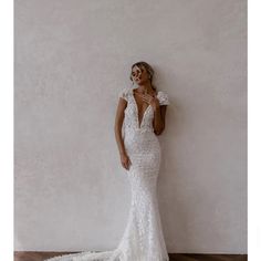 a woman standing in front of a white wall wearing a wedding dress with an open back