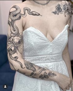 a woman wearing a white dress with tattoos on her arms and shoulder, holding a snake