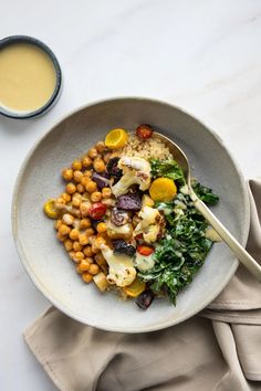 a white bowl filled with vegetables and chickpeas next to a cup of sauce