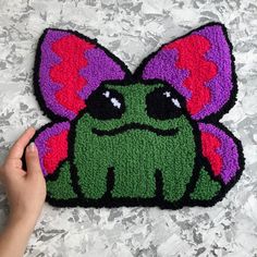 a hand is holding up a rug with a green and purple monster face on it