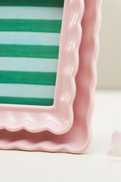 a pink and green frame sitting on top of a table next to a white flower