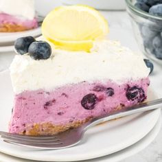 a slice of blueberry cheesecake on a plate with a fork and bowl of blueberries in the background