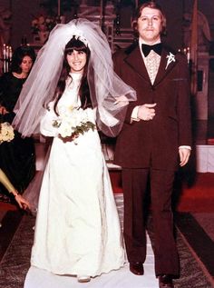 a man and woman in wedding attire standing next to each other on the aisle at a church