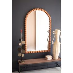 an oval shaped mirror sitting on top of a table next to a vase and lamp