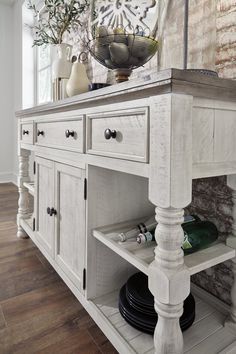 an old white buffet table with wine bottles on top and vases in the corner