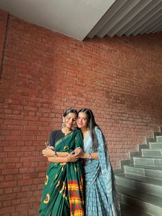 two women standing next to each other in front of a brick wall with stairs behind them