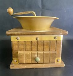 an old fashioned wooden bowl on top of a stand with drawers and knobs in front of a black background