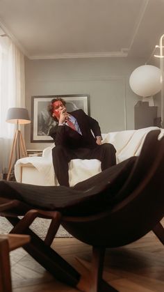 a man in a suit is sitting on a chair and talking on the cell phone