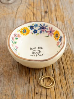 a wedding ring sits in front of a small bowl with the words love you to the moon and back on it