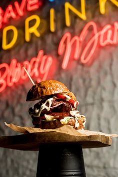 a large sandwich sitting on top of a wooden tray in front of a neon sign