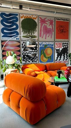 an orange couch sitting in front of a wall with posters on it's walls