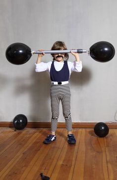 a young boy is holding two black balls above his head while standing on a hard wood floor