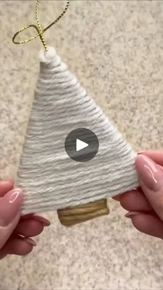 two hands holding an ornament that looks like a christmas tree with yarn on it