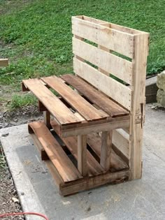 a bench made out of wooden pallets sitting on top of a cement slab next to a grass field