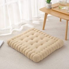 a beige dog bed sitting on the floor next to a table with a laptop computer