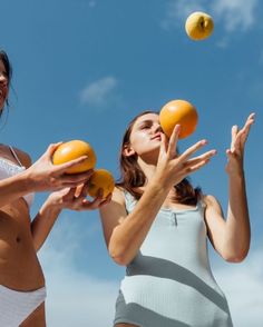 two women are playing frisbee on the beach in front of blue sky and clouds