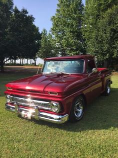 an old red truck is parked in the grass