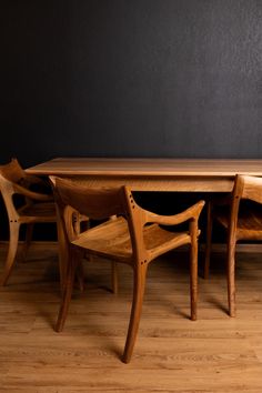 a wooden table with chairs around it on top of a hard wood floor next to a black wall