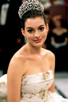 a woman in a white dress wearing a tiara and smiling at the camera while sitting down