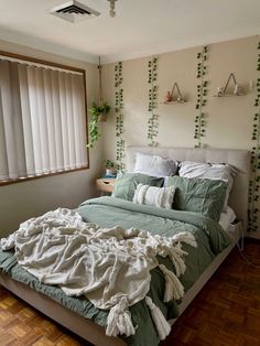 an unmade bed sitting in a bedroom next to a window with plants on the wall