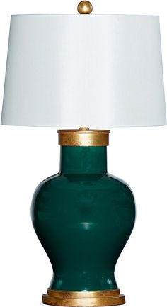 a green table lamp with a white shade on the top and gold trim around the base