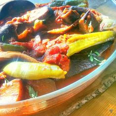 a glass bowl filled with vegetables on top of a wooden table next to a spoon