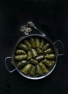 stuffed grape leaves in a pot with a spoon next to it on a black surface