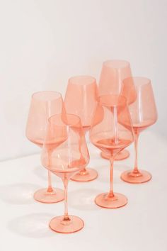 six pink wine glasses lined up on a white surface