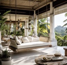 a porch with swings and hanging chairs on the side, surrounded by greenery in front of a large window