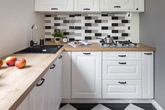 a kitchen with white cabinets and black and white checkered backsplash, wood counter tops