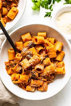 two white bowls filled with pasta and meat next to some parsley on the side