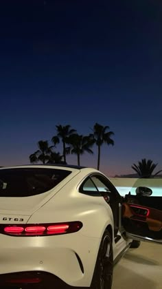 the rear end of a white sports car at night with palm trees in the background