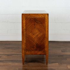 a small wooden cabinet sitting on top of a hard wood floor next to a white brick wall