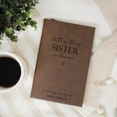 a book and cup of coffee sitting on top of a bed next to a plant