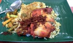 a green plate topped with rice and meat next to a silver spoon on top of a table