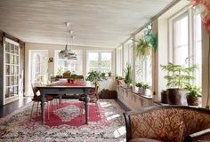 a living room filled with lots of furniture and plants on top of a red rug