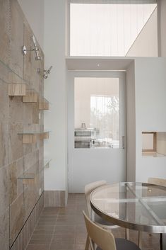 a dining room table and chairs in front of a glass wall with shelves on it