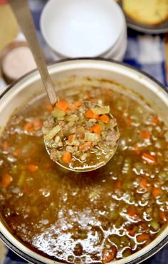 a ladle full of soup with carrots and other foods in bowls on the table