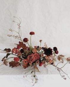 a bunch of flowers that are sitting on a white tablecloth with leaves and stems