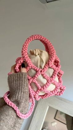 a hand holding a knitted purse with pink and white yarn on the handle, in front of a mirror