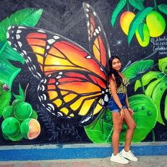 a woman standing in front of a wall with a butterfly painted on it