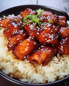 a black bowl filled with rice covered in sauce and topped with sesame seeds, garnished with green leaf