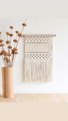 a vase filled with dried flowers next to a macrame wall hanging on the wall