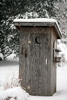 a outhouse in the middle of winter with snow on the ground and trees behind it