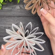 two hands holding paper flowers on top of a wooden table next to plants and scissors