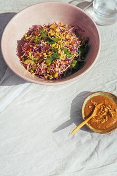 a pink bowl filled with salad next to a wooden spoon on top of a table