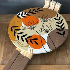 a wooden table topped with an orange and black flower painted on top of wood sticks