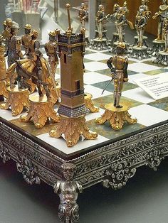 a chess set made out of gold and silver pieces on top of a checkered board