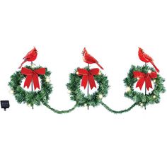 three red birds sitting on top of wreaths with bows and lights in the middle