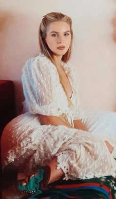 a woman sitting on top of a bed in a white dress